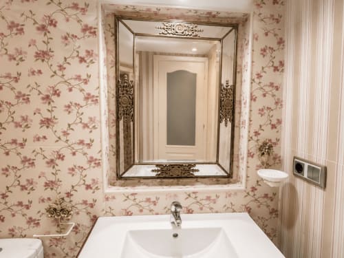 Baño elegante con papel tapiz floral, lavabo blanco y espejo enmarcado ornamentado en apartamento frente al mar de Holibai, Baiona