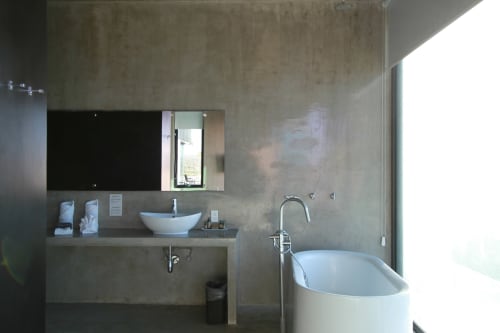 Baño moderno en suite frente al mar de Vidasoul con bañera soakable blanca, lavamanos tipo recipiente y paredes de hormigón con ventana con vista al mar