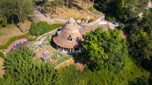 Aerial view of Le Paradis de Lucile B&B with conical roof, fire pit, loungers, and lush forest in La Roche Guyon