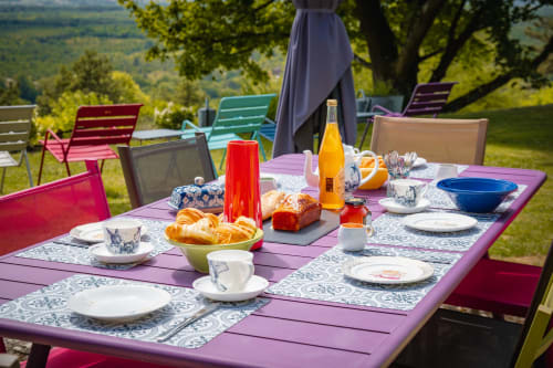 Outdoor breakfast setup at Le Paradis de Lucile near Giverny with purple table, colorful chairs, pastries, and valley views.