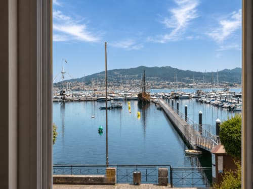 Vista panorámica del puerto de Baiona desde apartamento con veleros, marina y montañas al fondo