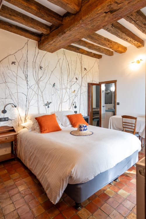Chambre rustique avec poutres apparentes, linge blanc, coussins orangés, fresque d'oiseaux, carrelage terracotta - Le Paradis de Lucile