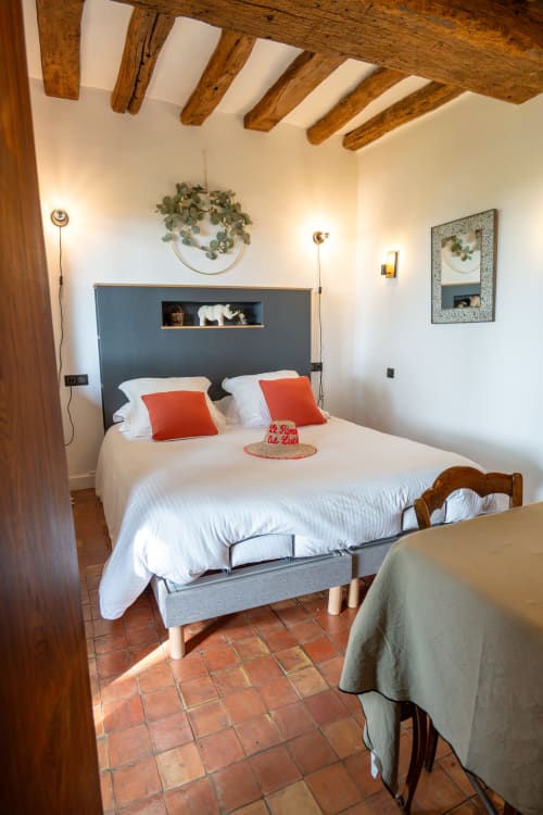 Chambre douillette au gîte Le Paradis de Lucile à La Roche Guyon avec poutres apparentes, tête de lit grise et coussins rouges