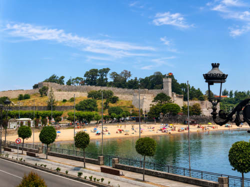 Frente marítimo de Baiona con murallas del castillo medieval, playa de arena y paseo costero en España