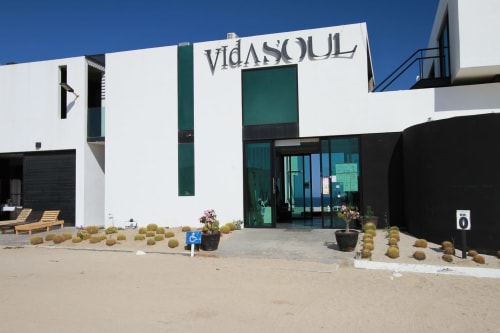 Cabaña frente al mar Vidasoul en La Vinorama con diseño moderno blanco y turquesa, entrada arenosa y vistas al mar