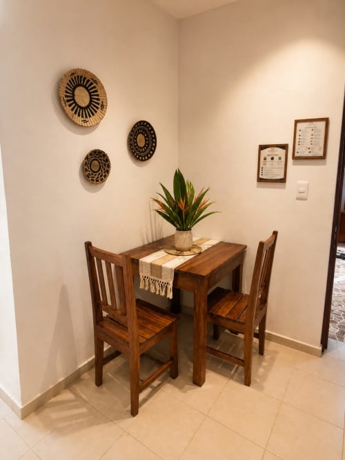 Mesa de comedor de madera con dos sillas en la suite del Hotel Isla Mujeres Centro, decorada con cestas tejidas en la pared y plantas en maceta