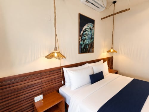 Habitación moderna del Hotel Isla Mujeres Centro con cama de marco de madera, ropa de cama blanca, lámparas colgantes y arte de aves en la pared