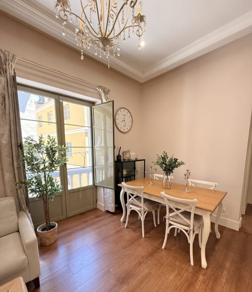 Elegante comedor con mesa de madera, sillas blancas, lámpara de cristal y balcón con vista al centro histórico de Málaga
