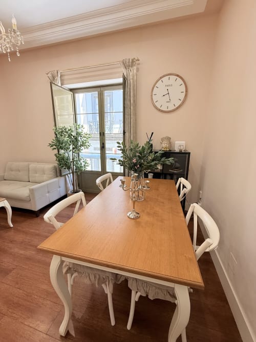 Elegante comedor en Madre de Dios Premium, Málaga con mesa de madera, sillas color crema, vistas a la ciudad y reloj parisino