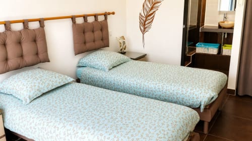 Twee eenpersoonsbedden met bedrooster en bruine gevoerde hoofdeinden in een kamer van Maison D'hôtes Coeur D'hérault, Péret