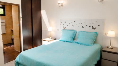 Lichte slaapkamer in cottage Péret met turquoise beddengoed, wit hoofdeinde met vlindersprookjes en tuinuitzicht