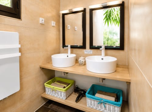 Modern badkamer met dubbele wastafel in Maison D'hôtes Coeur D'Hérault met beige tegels, rieten opberging en uitzicht op de tuin