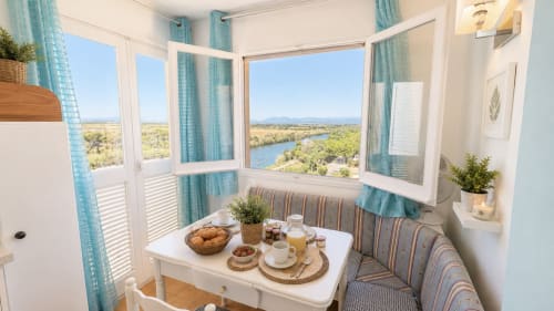 Apartamento luminoso con vista al río en Holidays Costa Brava, con cortinas turquesas, mesa de desayuno y vistas panorámicas
