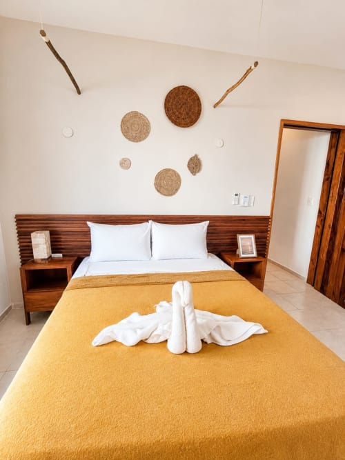 Habitación moderna del Hotel Isla Mujeres Centro con cama de madera, manta amarilla, almohadas blancas y decoración tejida en pared de Suite 6.