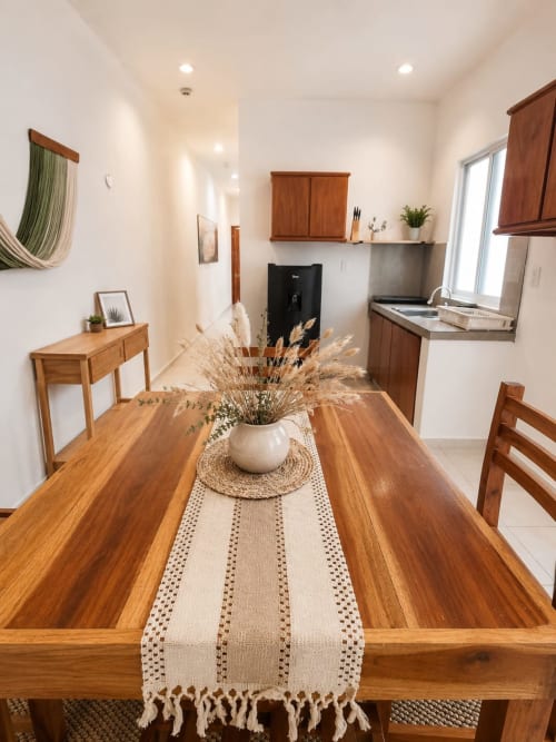 Cocina moderna con mesa de comedor de madera, paredes blancas, gabinetes de madera y electrodomésticos de acero inoxidable en Hotel Isla Mujeres