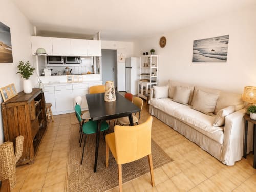 Appartement moderne à Lège Cap Ferret avec cuisine ouverte, salle à manger, table noire, canapé beige et mobilier bois.