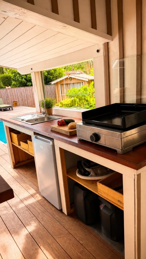 Cuisine extérieure de la villa La Loge Du Bassin avec plancha, évier, réfrigérateur et vue sur le jardin à Lège-Cap-Ferret