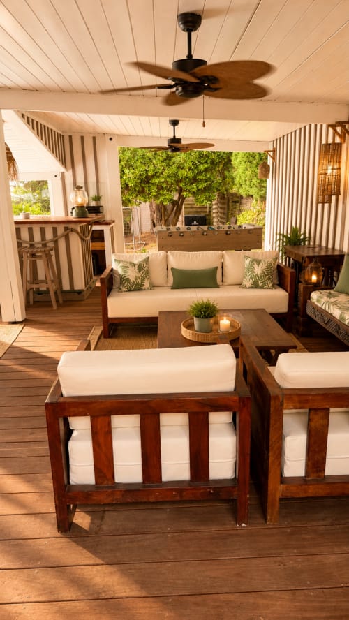 Lounge sous abri à la Villa La Chunga à Lège-Cap-Ferret avec mobilier en bois, coussins crème, ventilateur et vue sur la piscine
