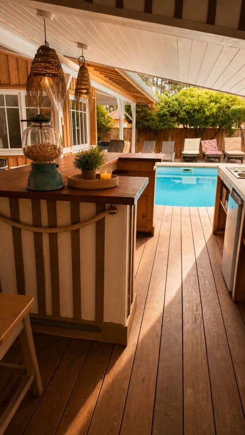 Terrasse couverte de la Villa La Chunga avec mobilier en bois, luminaires suspendus tressés et piscine chauffée surplombant un parc luxuriant