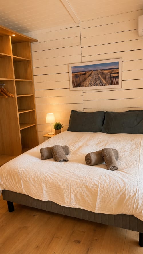 Chambre douillette à la villa La Loge Du Bassin à Lège-Cap-Ferret avec serviettes roulées, tête de lit noire, étagères en bois et plage