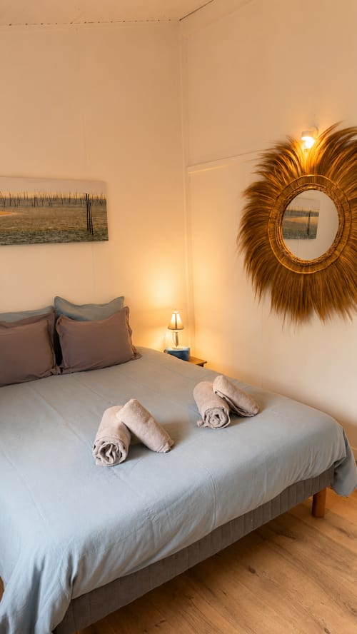 Chambre élégante de la villa La Loge Du Bassin à Lège-Cap-Ferret avec serviettes roulées, miroir soleil doré et ambiance chaleureuse