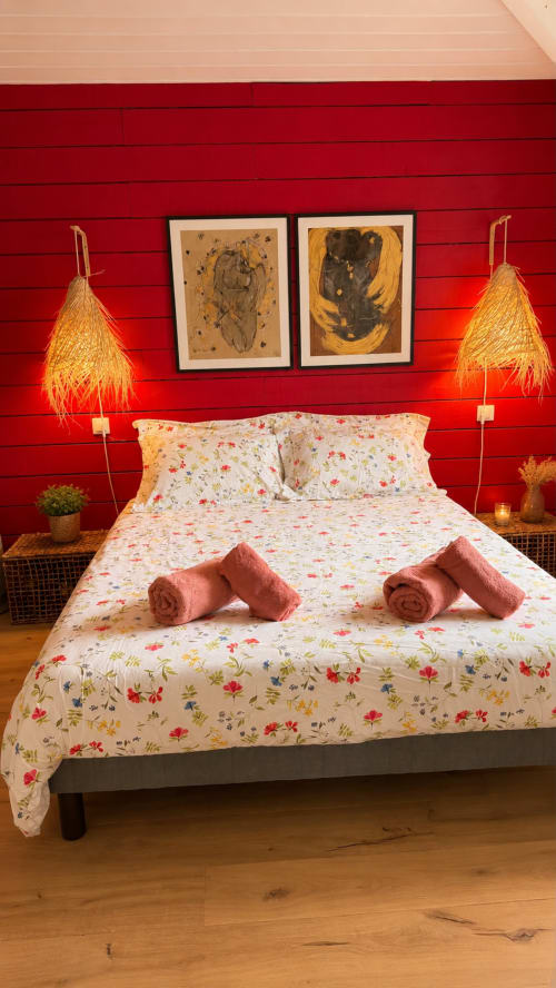 Chambre douillette aux murs rouge vif, literie florale, serviettes roses roulées, lampes suspendues tressées et tableaux encadrés à La Loge Du