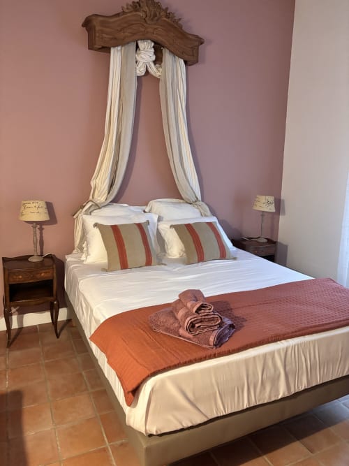 Lit à baldaquin élégant avec coussins rayés et serviettes pliées dans la chambre du gîte Entre Ciels et Lettres, Grignan