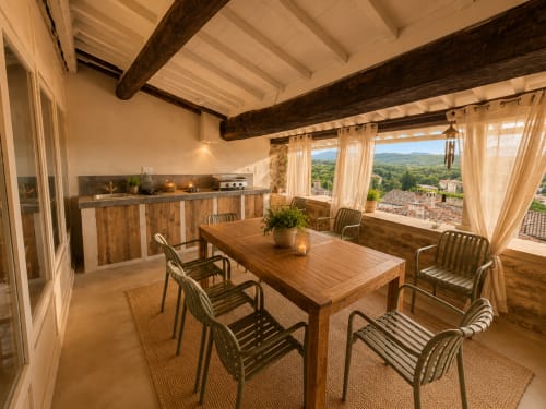 Terrasse ensoleillée d'Entre Ciels et Lettres à Grignan, avec table de bois, chaises, cuisine et vue sur les montagnes