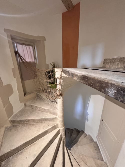 Escalier en pierre avec rampe en bois au cottage de Grignan, menant à l'étage avec murs blancs et mur d'accent en terre cuite
