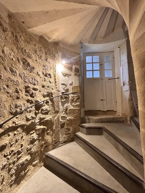 Escalier en pierre avec rampe métallique noire menant à une porte blanche à l'entrée du gîte de Grignan, lumière chaleureuse