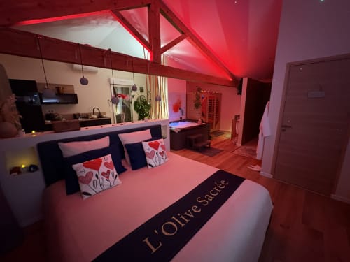 Chambre de la Suite L'Olive Sacrée avec éclairage rose, lit king size, coussins en forme de cœur rouge et équipements spa à Cabannes, Provence