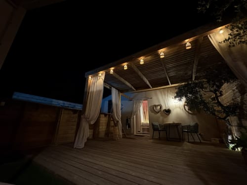 Terrasse illuminée de Suite l'Olive Sacrée en Provence avec pergola, voilages blancs et salon de jardin en soirée