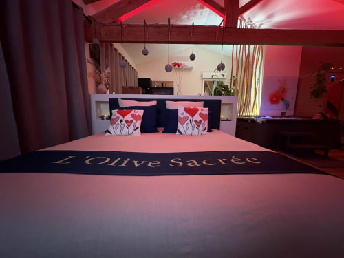 Suite luxueuse avec literie rose, branding 'L'Olive Sacrée', coussins décor et éclairage ambient rouge