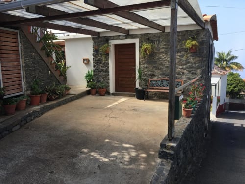Private patio entrance of BHF Residences apartment in Arco da Calheta with dark wood door, pergola, potted plants, and stone
