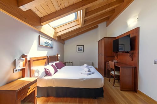 Bright double bedroom at Casa Azcona with wooden beams, skylight, TV, desk, and mountain views in Zizur Mayor