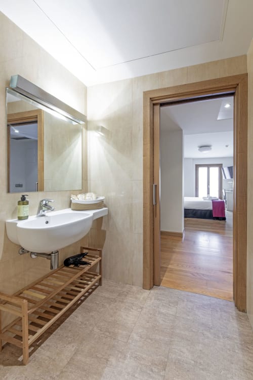 Modern bathroom at Casa Azcona hotel in Zizur Mayor with white sink, mirror, wooden accents and view to bedroom