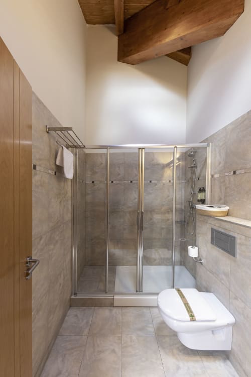 Modern bathroom in Casa Azcona hotel with glass shower enclosure, white toilet, beige tile walls, and exposed wooden ceiling