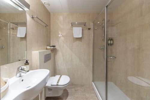 Modern bathroom at Casa Azcona hotel with white sink, toilet, glass shower enclosure, and beige tile walls in Zizur Mayor