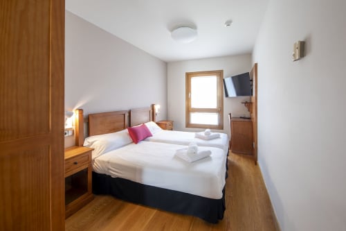 Chambre twin à l'hôtel Casa Azcona à Zizur Mayor avec mobilier en bois, literie blanche, télévision et vue montagne