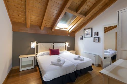 Chambre double avec poutres en bois apparentes, lits blancs, mur d'accent sombre et puits de lumière à l'hôtel Casa Azcona de Zizur Mayor