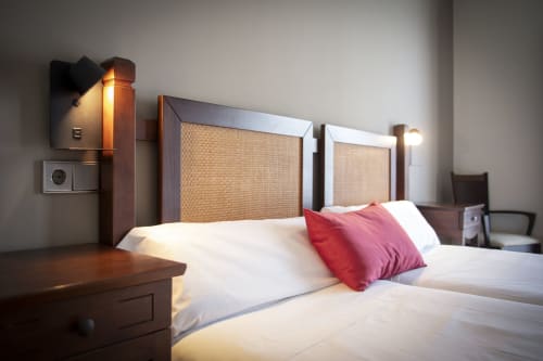 Chambre double à Casa Azcona avec deux lits, oreiller rouge, tête de lit en bois, éclairage moderne et mobilier contemporain