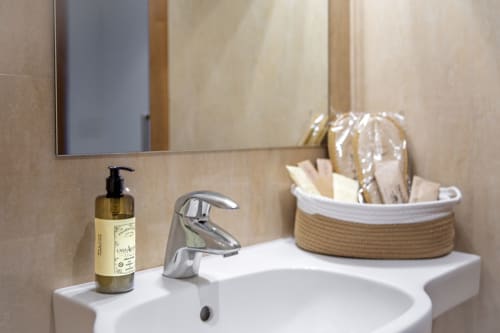 Lavabo moderne à l'hôtel Casa Azcona avec distributeur de savon, robinetterie chromée, miroir et panier tressé d'accessoires