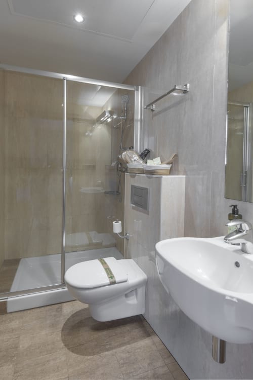 Salle de bain moderne de l'hôtel Casa Azcona avec lavabo blanc, toilettes, douche vitrée et carrelage gris