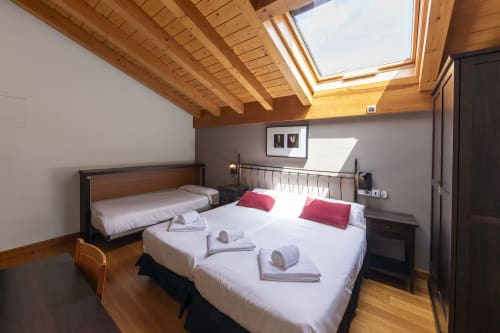 Chambre triple lumineuse à Casa Azcona avec poutres en bois apparentes, puits de lumière et deux lits aux oreillers rouges