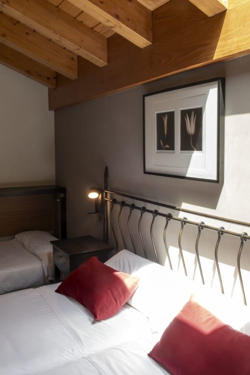 Chambre moderne de Casa Azcona avec poutres en bois apparentes, literie blanche, oreillers rouges et vue sur les montagnes