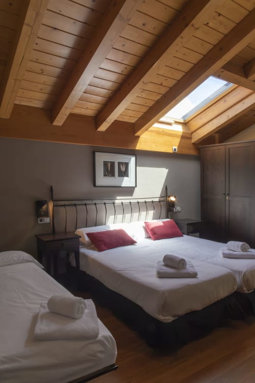 Chambre mansardée lumineuse à Casa Azcona avec poutres apparentes, puits de lumière, lit en métal, coussins rouges et vue sur les montagnes