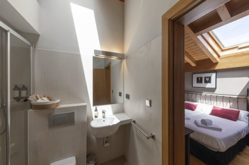Salle de bain moderne avec douche et lavabo à l'hôtel Casa Azcona à Zizur Mayor, Espagne, avec chambre visible par la porte