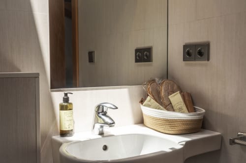 Lavabo moderne de l'hôtel Casa Azcona avec vasque blanche, robinetterie noire, distributeur de savon et panier tressé