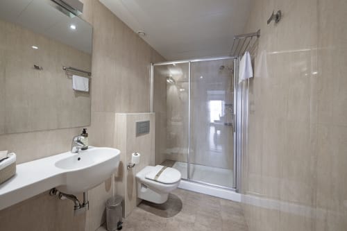 Salle de bain moderne de l'hôtel Casa Azcona avec lavabo blanc, toilettes et douche vitrée aux murs carrelés beige