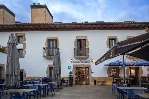 Cour intérieure de l'hôtel Casa Azcona à Zizur Mayor avec façade blanche, détails en pierre, sièges bleus et parasols